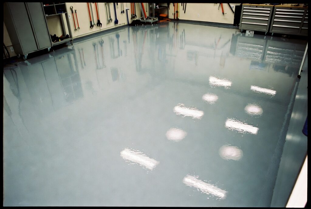 Clean garage with glossy grey epoxy floor coating reflecting lights, tools neatly stored, bright light