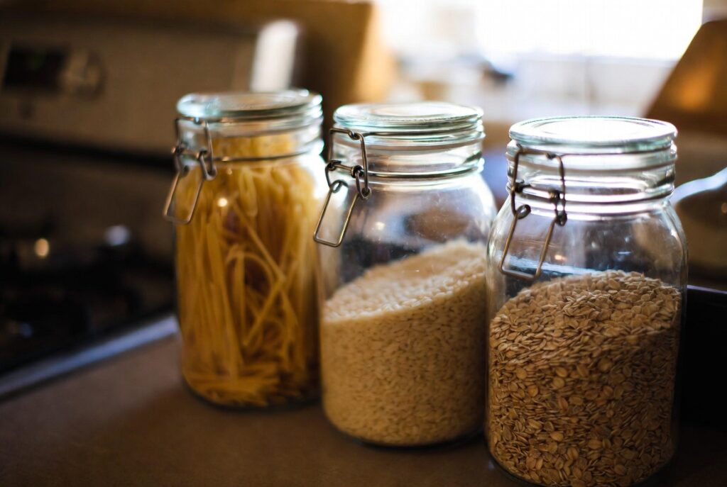 Matching glass canisters with decanted pasta rice and oats on kitchen counter, warm natural light, organized pantry style