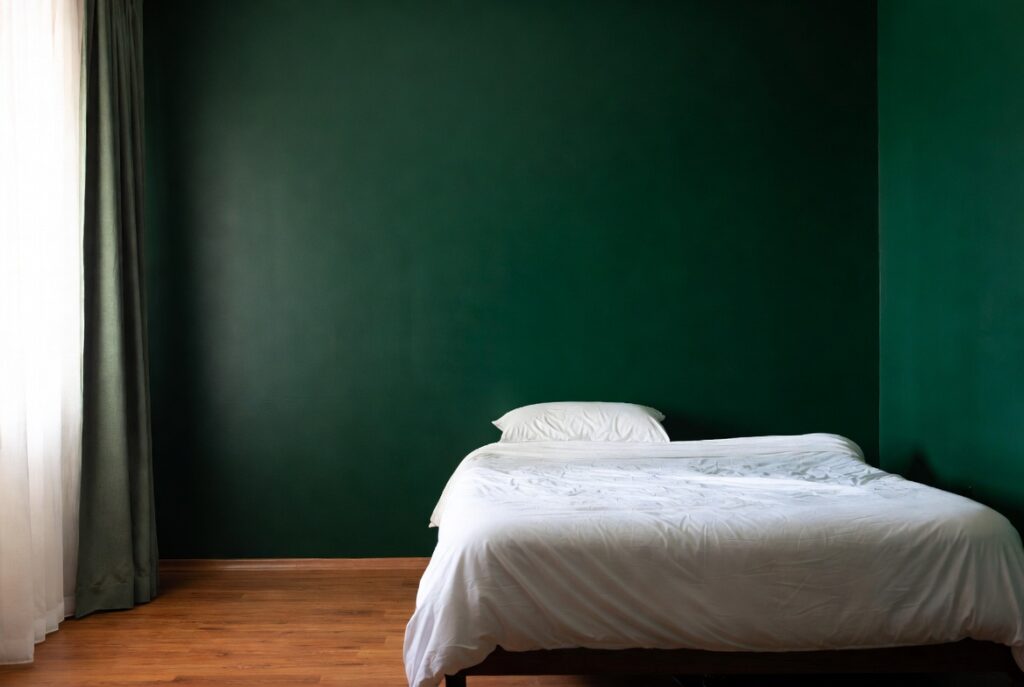 Bedroom with deep forest green accent wall behind bed, warm wood floors, white bedding, natural light