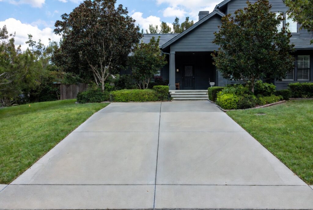 Freshly edged clean concrete driveway with border plantings, manicured lawn edges leading to home entrance, natural light