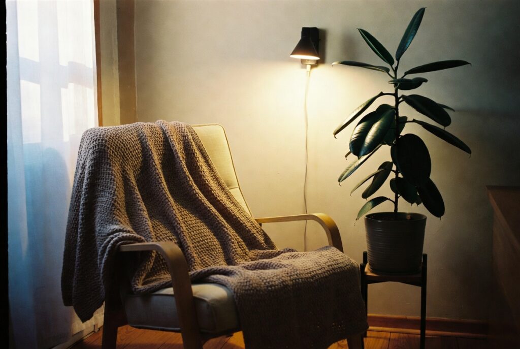 Cozy wellness reading corner with comfortable chair, soft light, plant and throw blanket, calm natural light