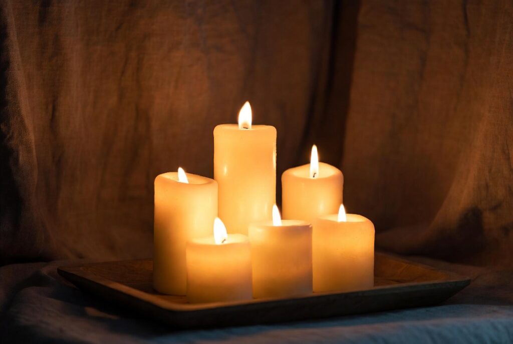 Cluster of lit candles at varying heights on wooden tray creating warm flickering atmosphere, cozy evening glow