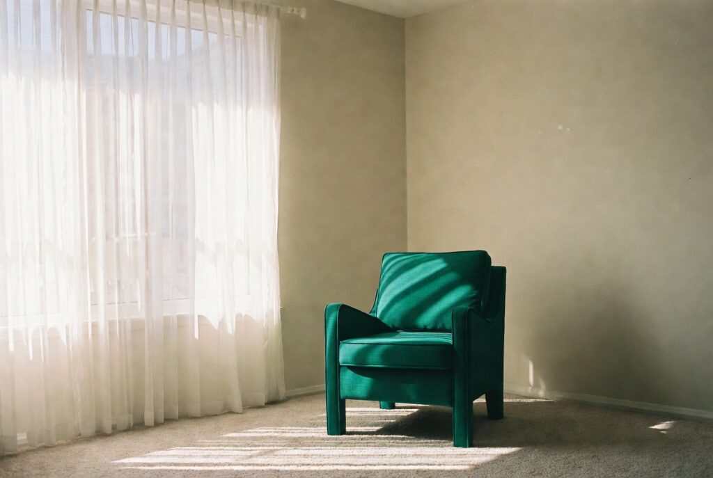 Neutral living room with bold emerald green accent chair as striking focal point, natural light, candid shot