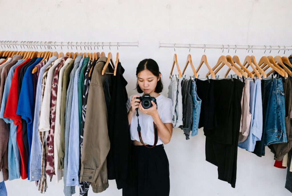 Person photographing wardrobe items on hangers against white wall for digital inventory, natural daylight, candid shot