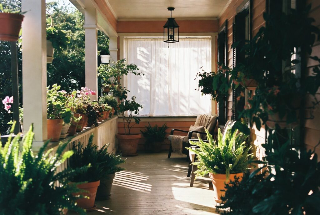 Fresh welcoming spring porch with potted plants, lantern and comfortable chair in warm daylight, candid shot