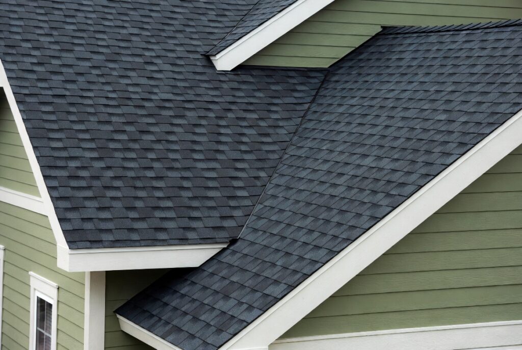 Home with dark charcoal architectural shingle roof contrasting warm sage green siding and white trim, natural daylight