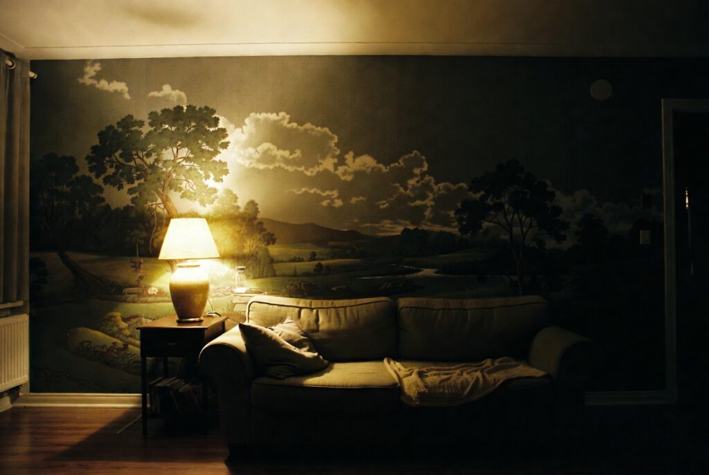 Living room with deep moody scenic wallpaper feature wall behind sofa, warm ambient light, candid shot