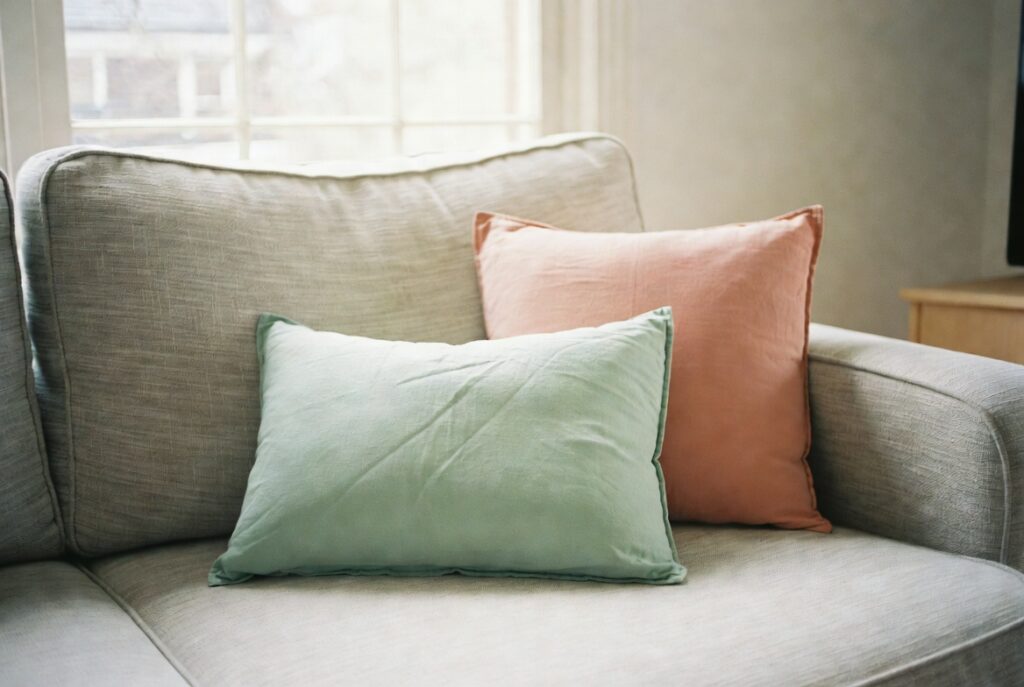 Living room with soft mint green and pale coral accent cushions on neutral sofa, bright spring light