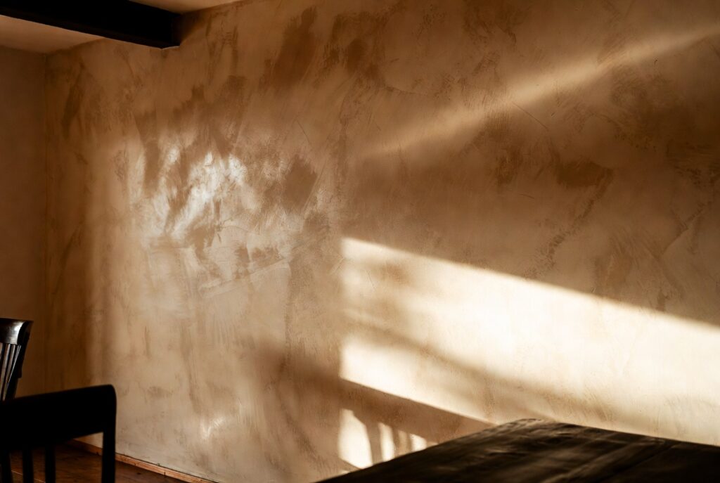 Dining room wall with layered Venetian plaster in warm sand tones catching raking light, natural light