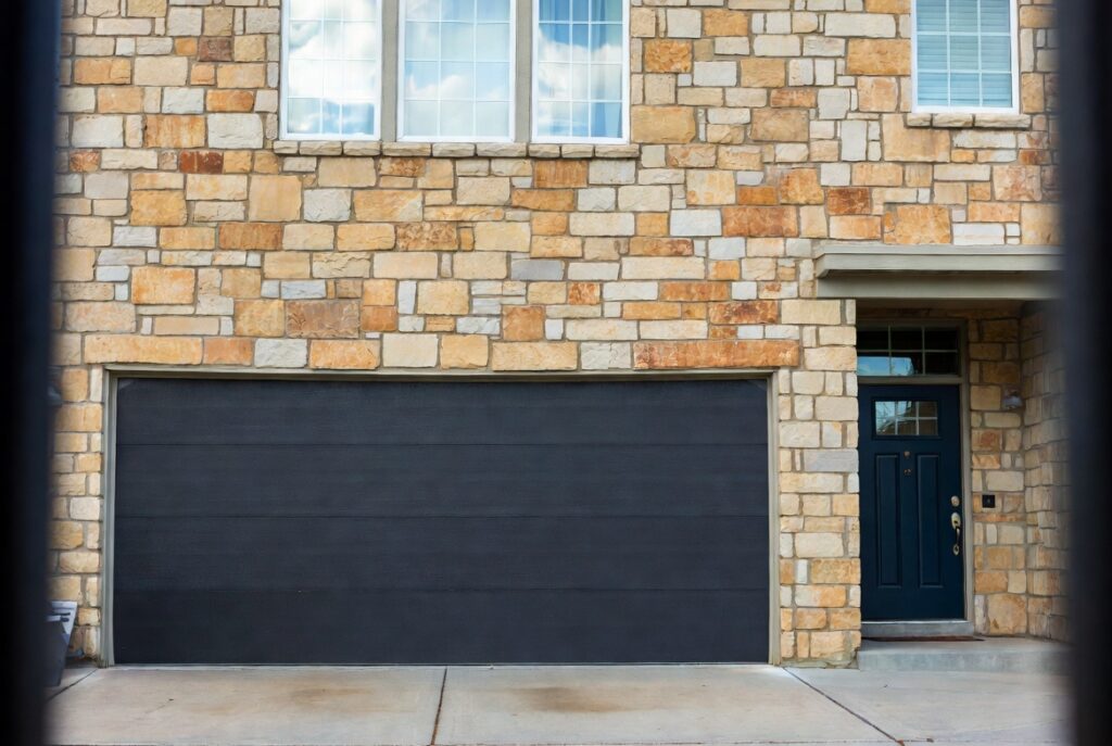 Modern home with dark charcoal garage door coordinating with navy front door and warm stone facade, natural daylight