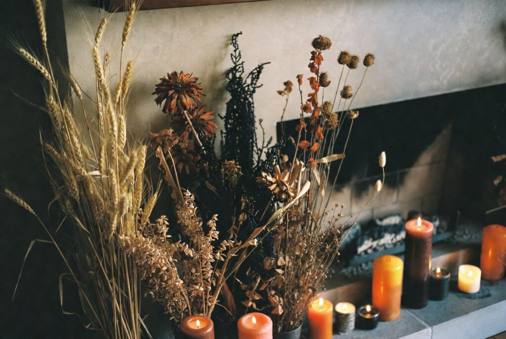 Styled autumn fireplace mantel with dried botanicals, candles and warm-toned decor at varying heights, cozy glow