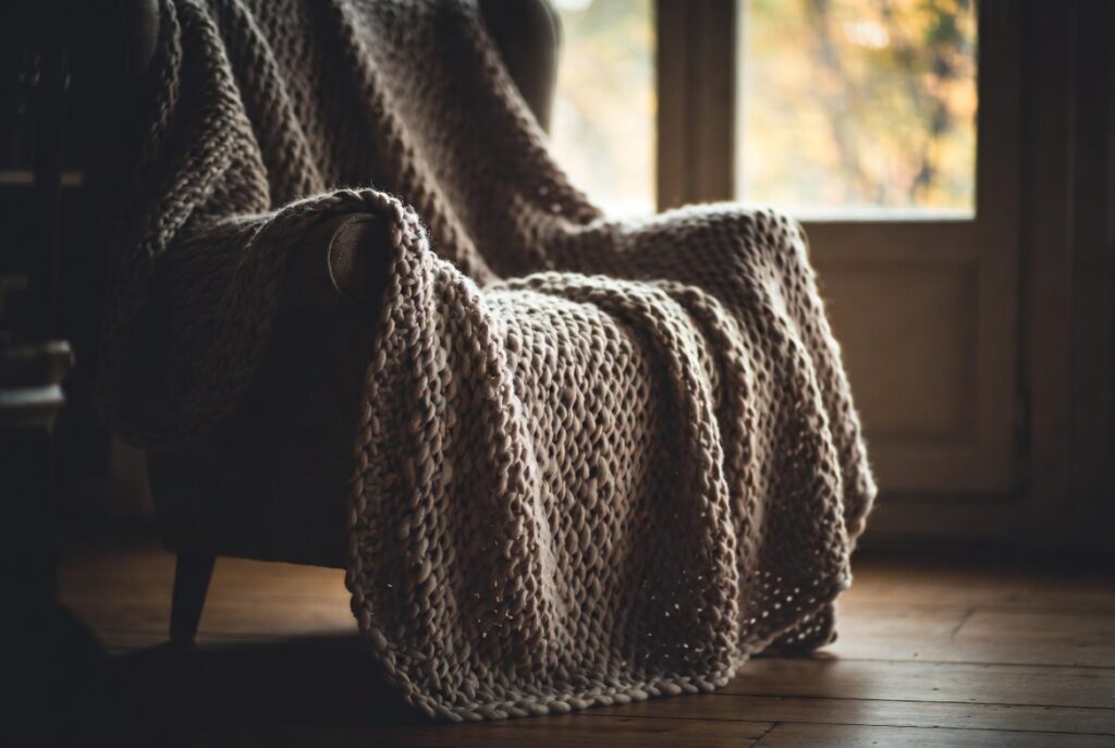 Oversized chunky knit throw draped casually over armchair in cozy autumn room, soft warm light