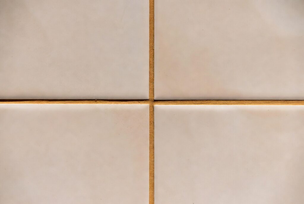 Close-up bathroom tile with warm sand-toned grout lines between large format cream tiles, natural light, sharp detail