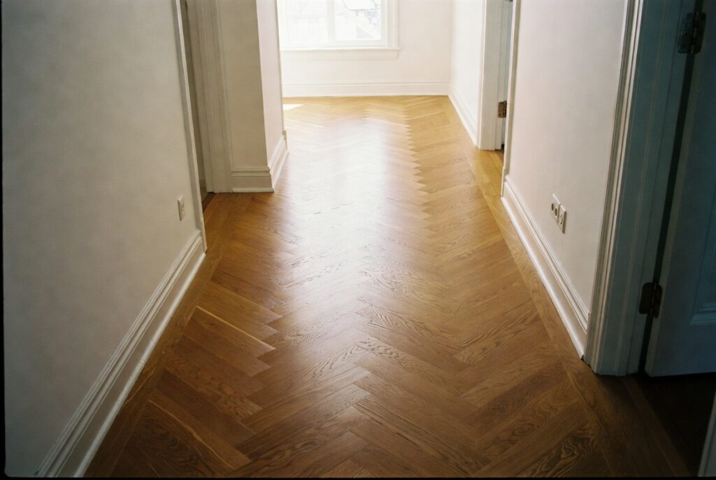 Hallway with stunning herringbone oak wood floor in warm amber tones, natural daylight, elegant home interior