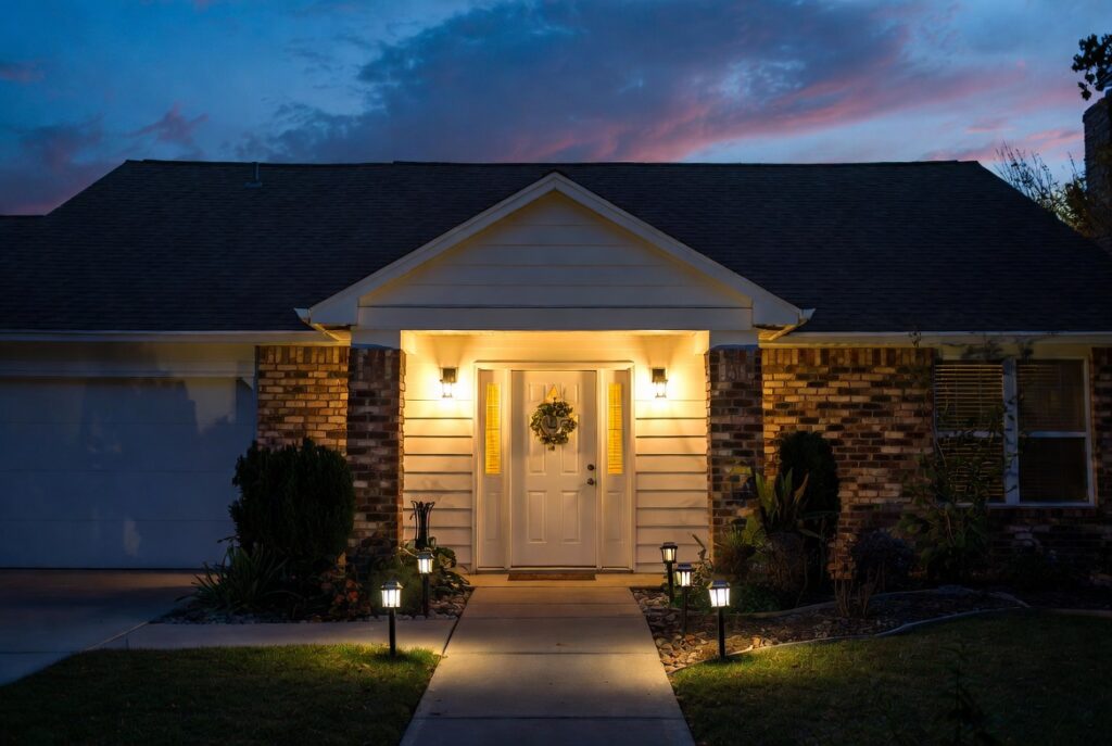 Home exterior at dusk with warm wall sconces flanking front door and glowing solar path lights on walkway