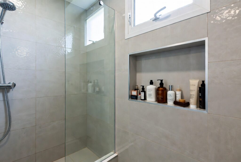 Modern bathroom with recessed wall niche holding toiletries neatly beside frameless shower, natural light, organized design