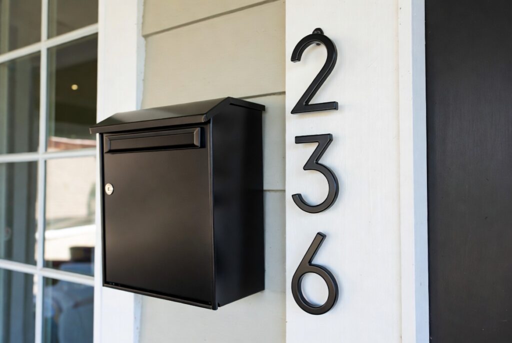 Close-up powder-coated matte black mailbox with coordinated house numbers on modern home exterior, natural daylight