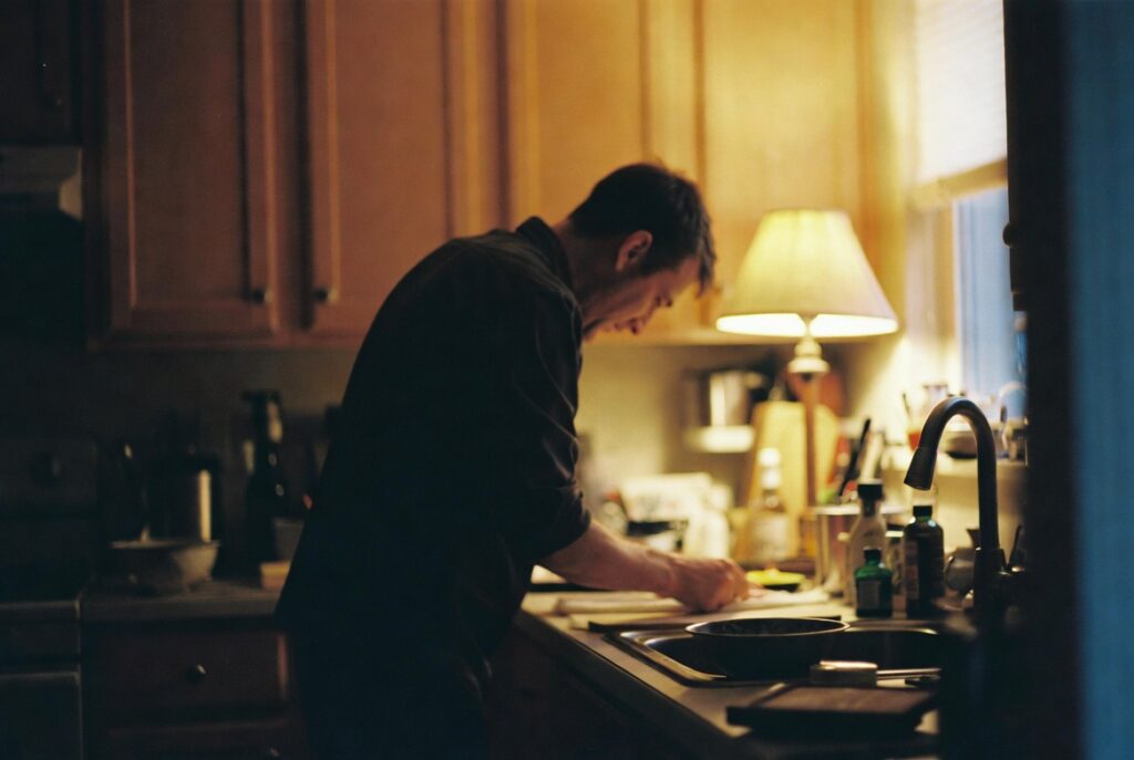 Person doing quick evening surface reset in tidy kitchen by warm lamp light, candid home organization moment