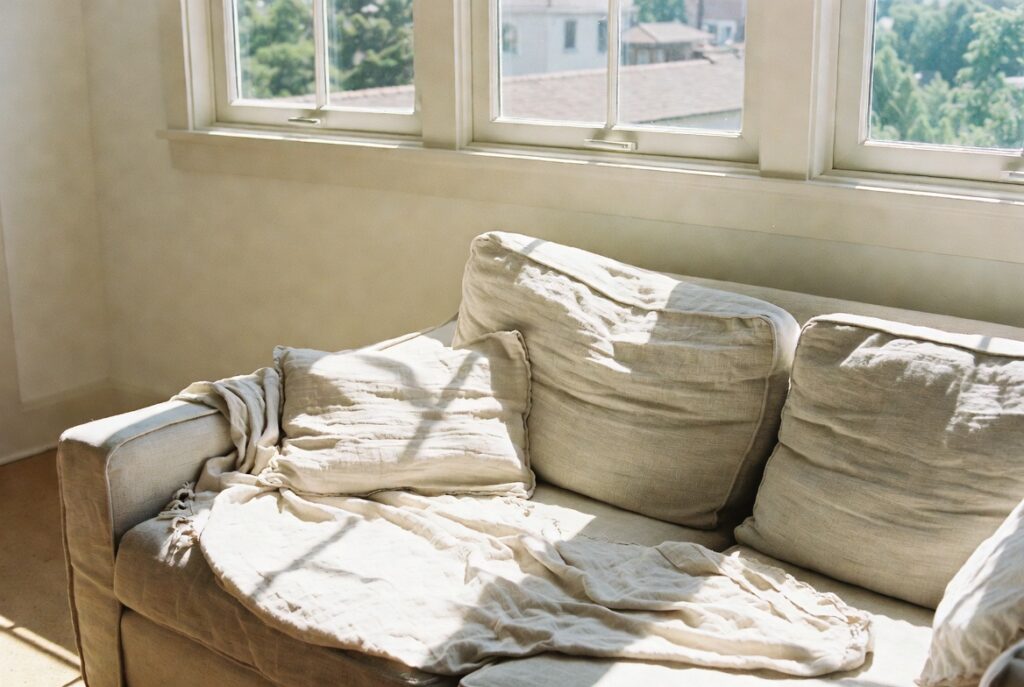 Bright living room with light linen cushions and airy cotton throw on sofa near sunny window, soft natural light