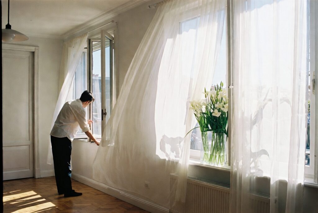 Person opening windows and placing fresh flowers in sunlit bright room during morning refresh, natural light, candid shot