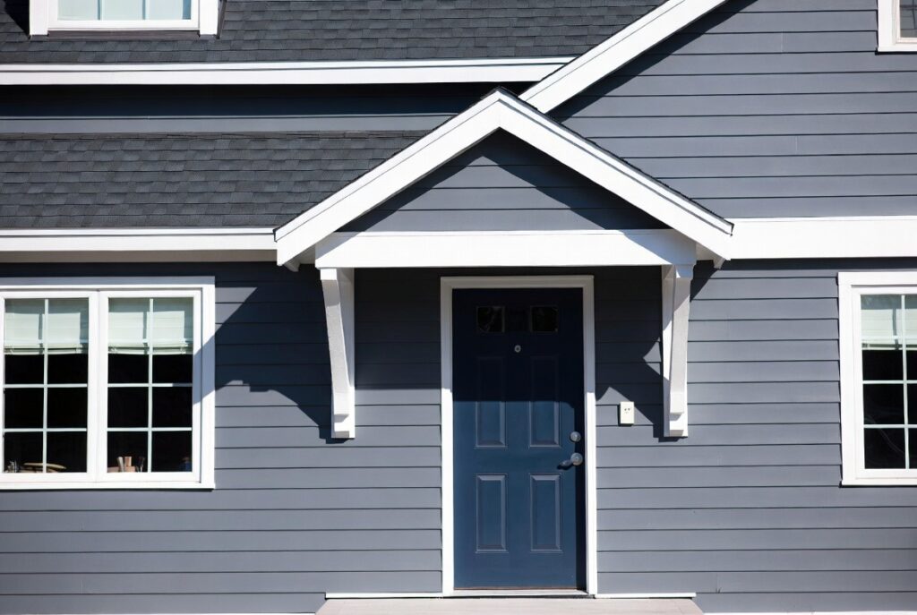 Home exterior with crisp white trim contrasting warm grey siding and navy blue front door, afternoon light