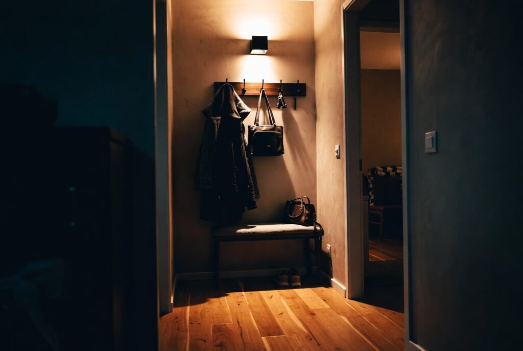 Tidy entryway with wall-mounted hook rail holding coats bags and keys beside small bench, warm light, organized home