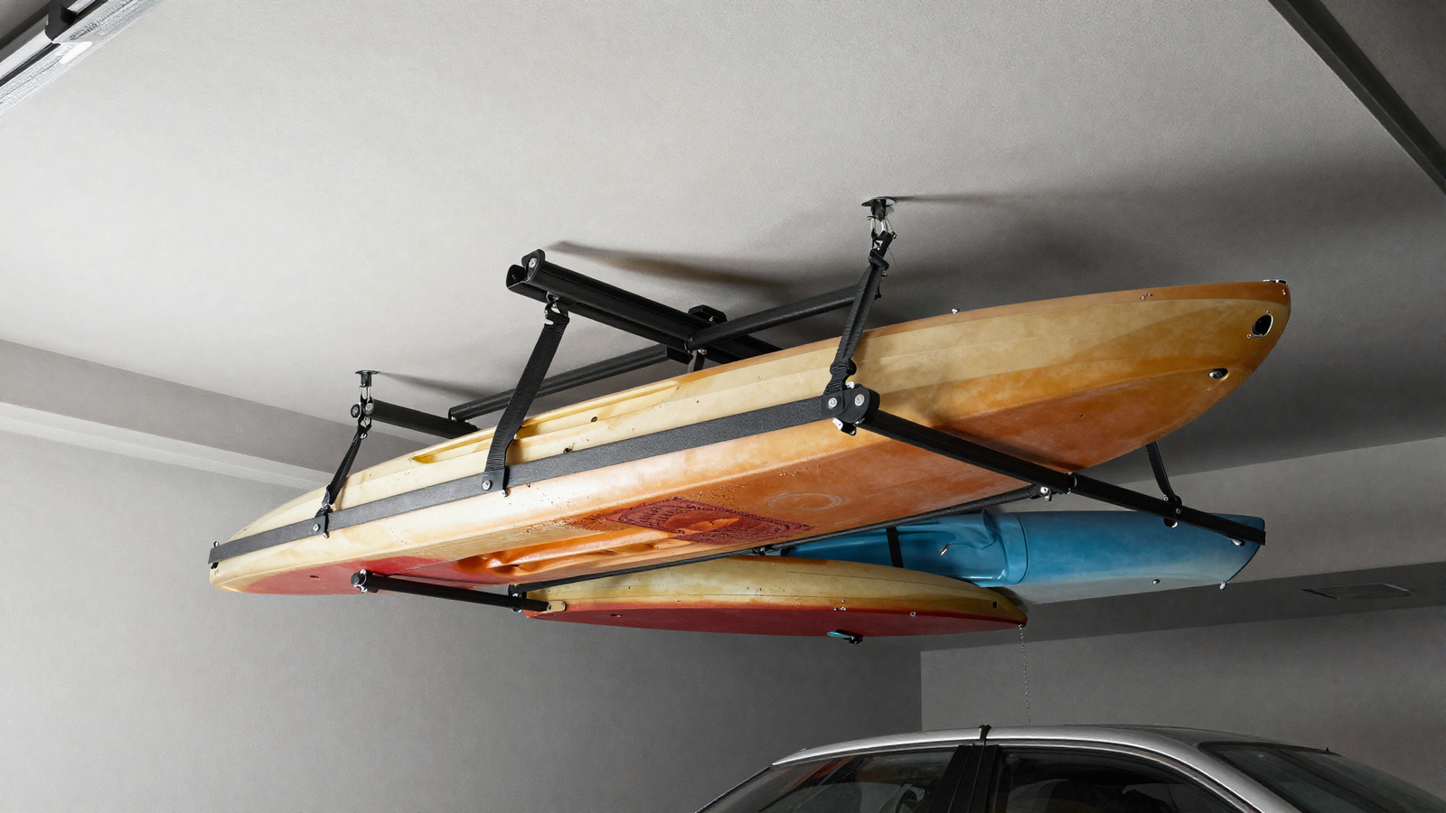 Ceiling-mounted kayak and sports gear lift system above garage parking space