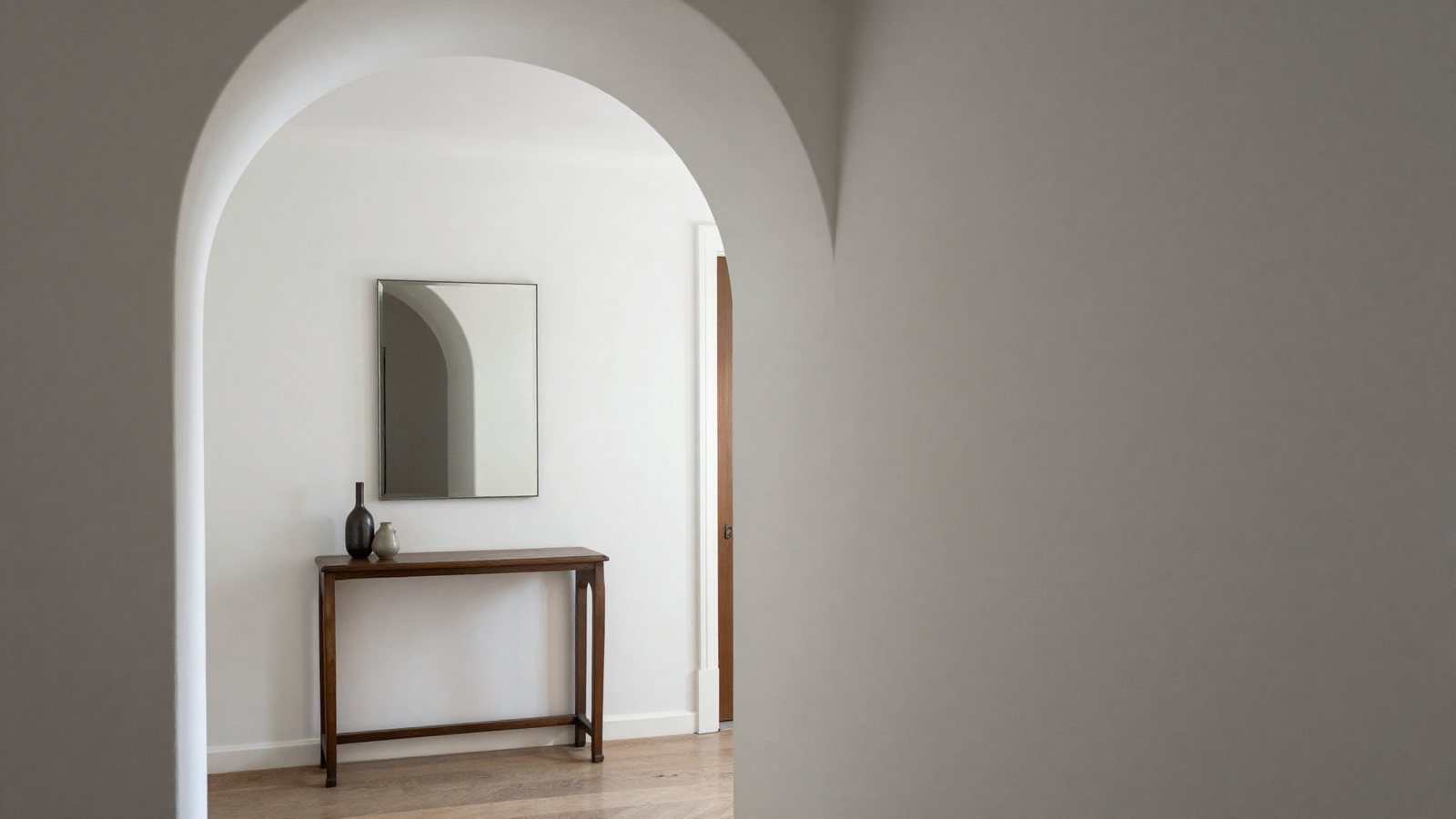 Hallway with white arched doorway framing a styled vignette of console table and mirror