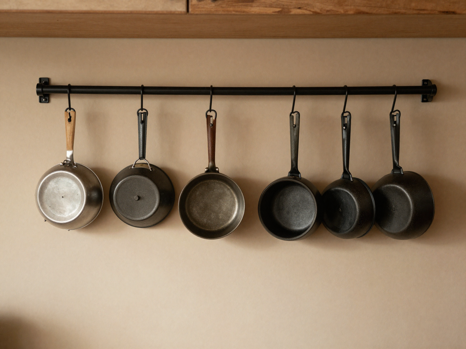 Black metal wall rack holding hanging pots and pans in kitchen