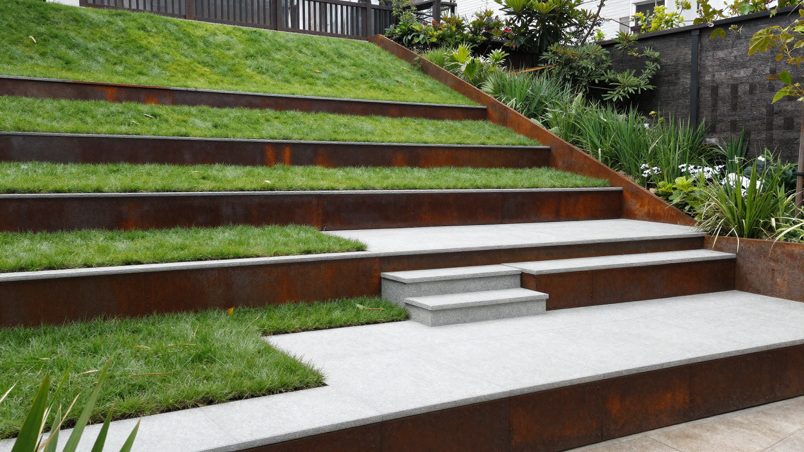 Multi-level sloped backyard with tiered lawn split patio and corten steel edging