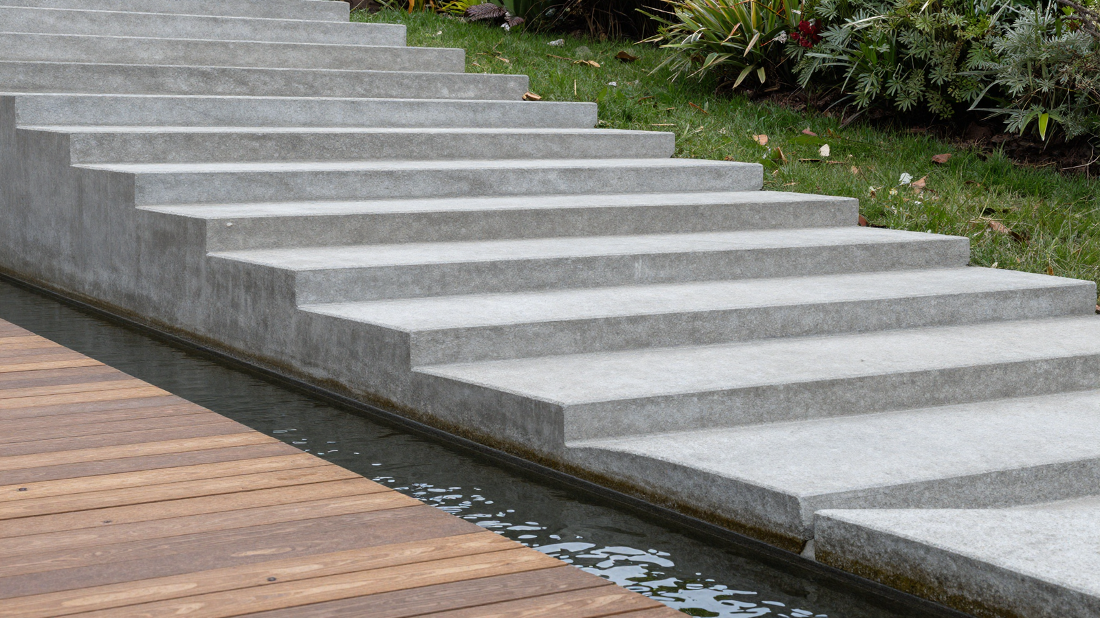 Concrete terrace steps climbing a sloped backyard with a narrow water channel