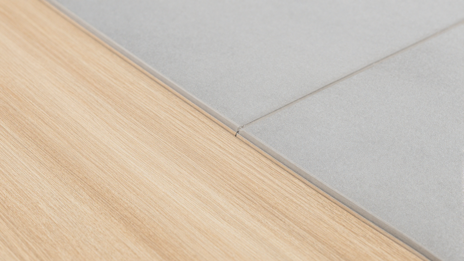 Close-up of flush floor transition between light wood flooring and gray tile with a thin color-matched seam
