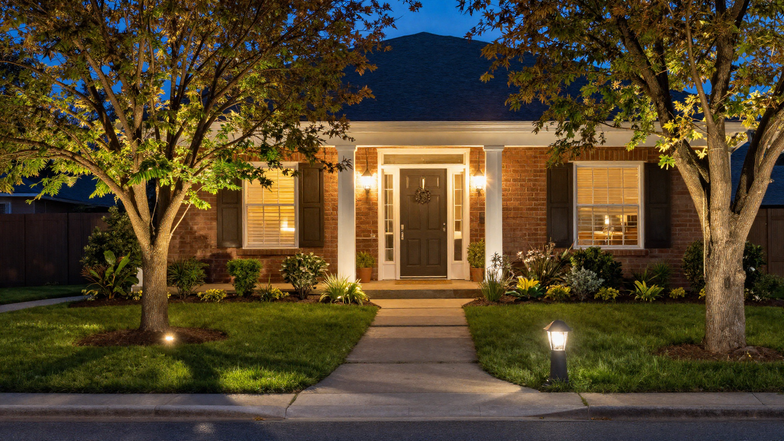 Full nighttime front yard view combining tree uplighting walkway lights and porch lanterns