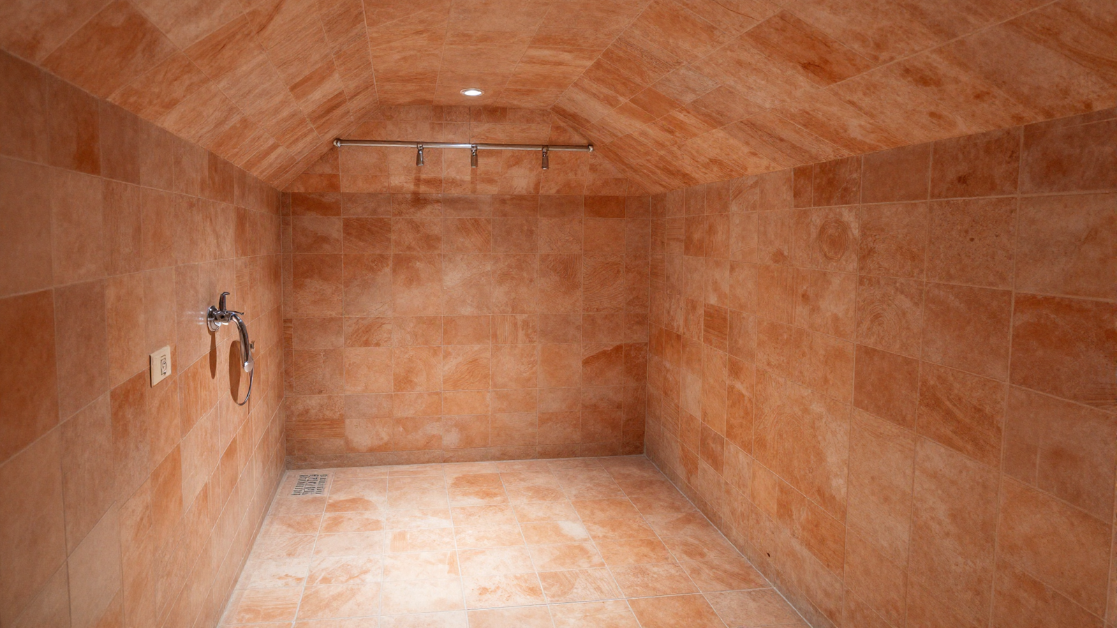 Bathroom shower with tile extending up and across the ceiling in continuous terracotta wrap