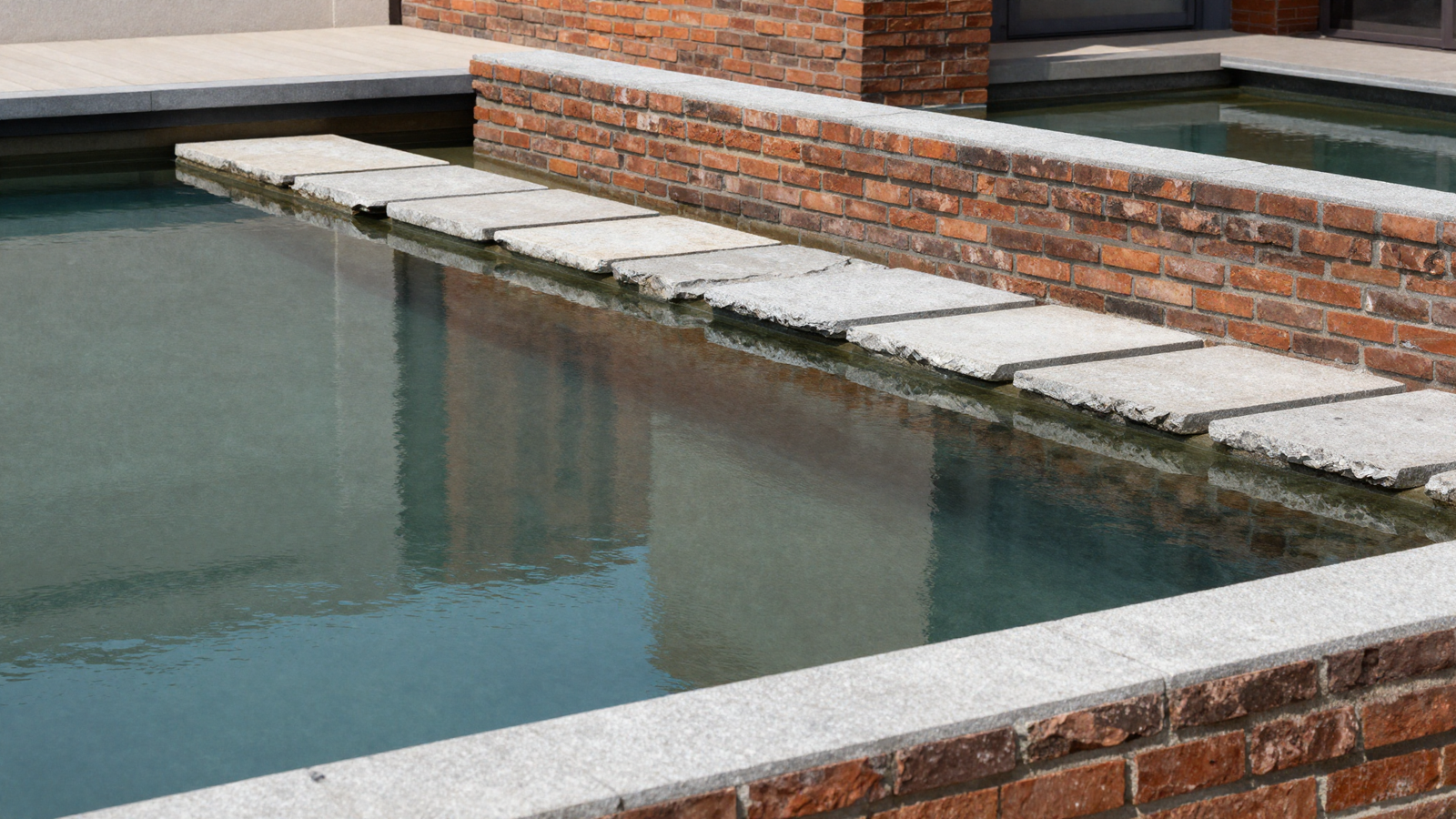 Brick-framed reflecting pond with stepping stone path across the surface