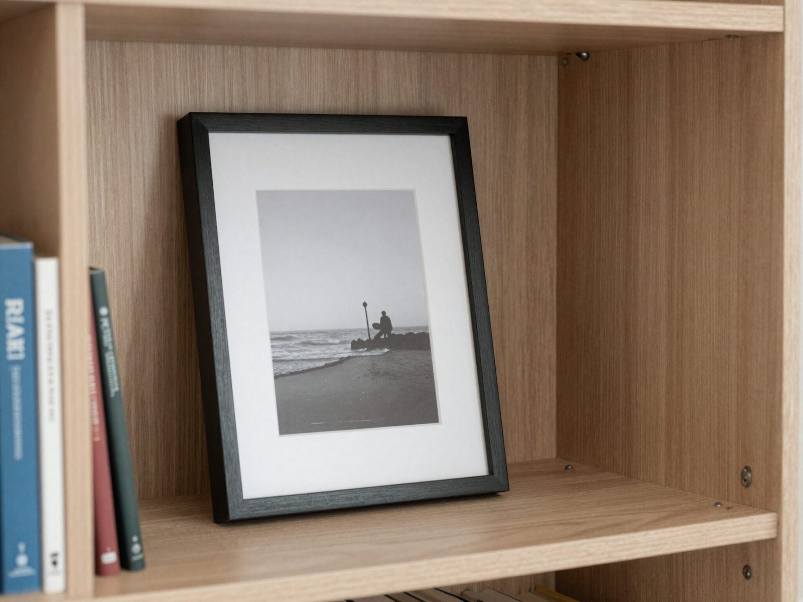 Small framed art print leaning casually against the back panel of a bookshelf