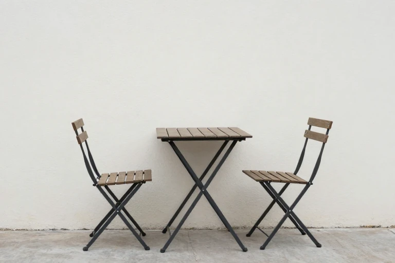 A folding bistro table and chairs tucked against a garden wall.