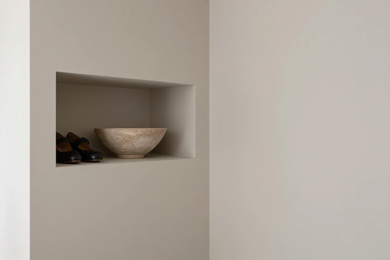 A hallway nook with a recessed shelf holding shoes and a decorative bowl.