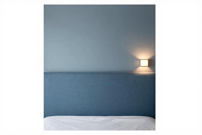 A bedroom with a soft blue accent wall, a plush fabric panel, and a dimmable wall sconce.