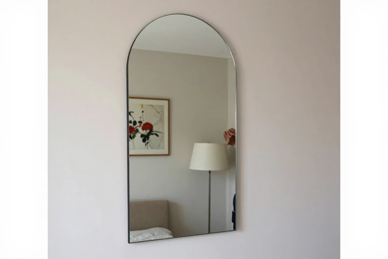Arched mirror angled to reflect a lamp and floral artwork