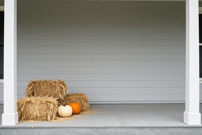 Hay bale and wheat sheaves arranged on a porch step with a pumpkin nearby.